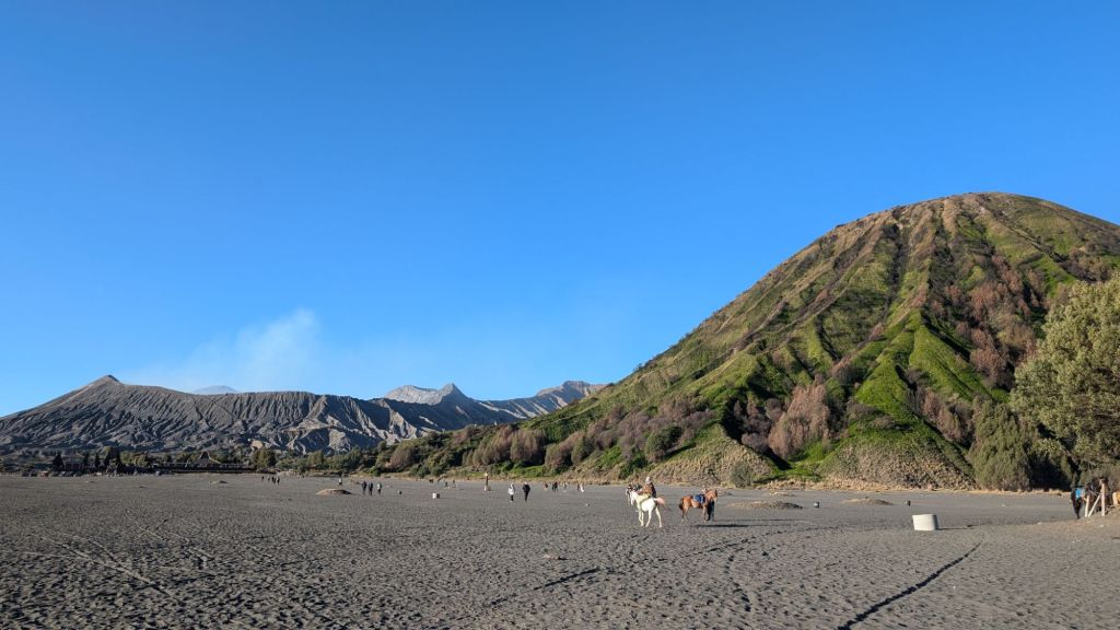 the sandy ground of the sea of sands at the foothills of mount bromo crater and active volcano in the distance