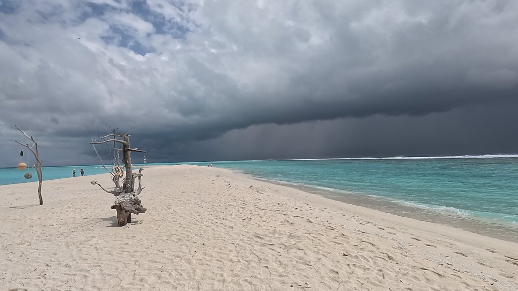 dark black clouds approach the white sandbar at the end of fulhadhoo island

